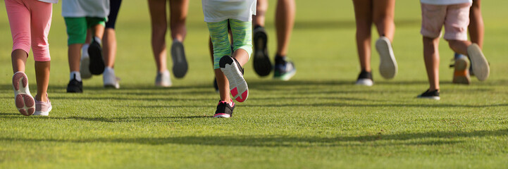 Fototapeta premium Running children, young athletes run in a kids run race, running on grass detail on legs, running in the light of morning 