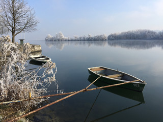Fischerboote liegen festgemacht am Flussufer mit raureif-überzogenen Bäumen und Pflanzen
