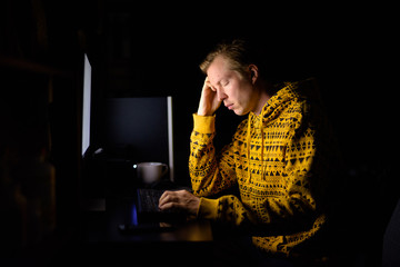 Stressed young man looking tired while working overtime at home in the dark
