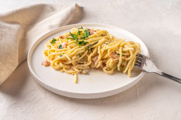 Classic homemade pasta carbonara Italian with bacon, eggs, parmesan cheese on light ceramic plate with fork and napkin on light table. Close up view