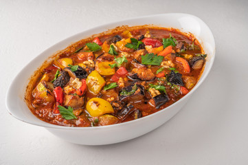 Homemade vegetable stew of eggplant, zucchini, tomatoes, peppers, garlic, prunes and greens on bowl on light background. Close up