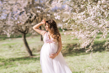 Fototapeta na wymiar beautiful pregnant woman in a long light dress walks in a blooming spring garden.