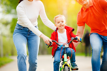 Family activities summer day. Happy mom and father learning little kid son to ride bicycle