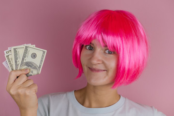 emotional portrait of a young beautiful happy woman with pink hair holding dollars on a pink background