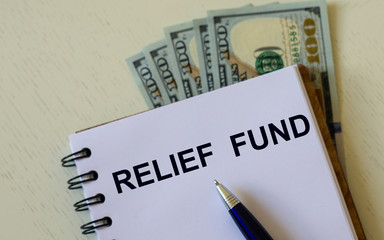 Obraz premium RELIEF FUND words in a notebook with a pen against the background of dollar bills
