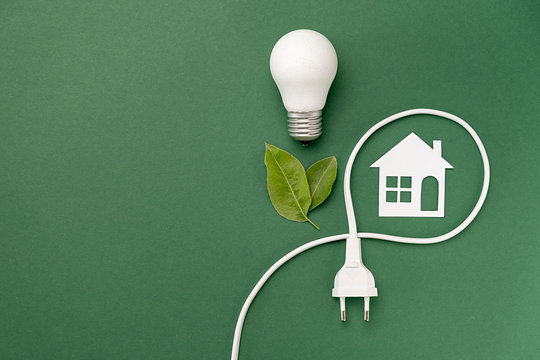 Concept for saving energy, eco-friendly, global warming. Creative top view flat lay of LED light bulb, electrical plug, leaves, paper house composition with copy space on green background