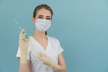 woman doctor in mask and gloves holds a syringe in hand on a blue background