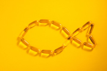 Shape of fish made with cod liver oil capsules on orange background