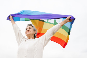 Low angle view of a old woman holding waving LGBT flag over head.  LGBT concept and old age.  white background