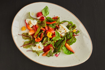 Vegetarian salad with strawberries, bell peppers, Basil and mozzarella, dressed with olive oil in a white plate on a white background.