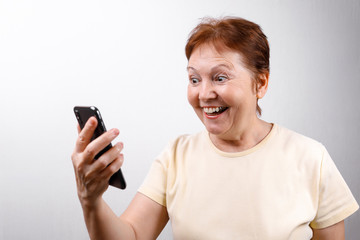 senior woman looks in surprise at the phone on a white background in a light T-shirt. place for text, isolated