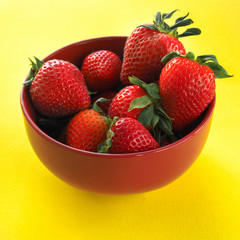 Ripe juicy and fragrant strawberries in a ceramic bowl on a bright yellow background