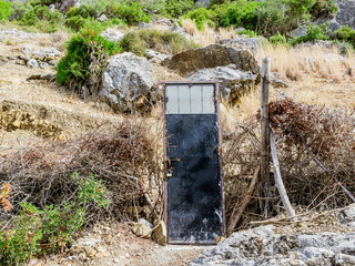 Iron door in the midst of a shattered dried hedge. Metal door on an empty mountains. Absurd...