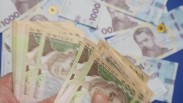 A man quickly counts banknotes of 500 Ukrainian hryvnia on the background of banknotes nominal value of 1000 hryvnia, close-up shot