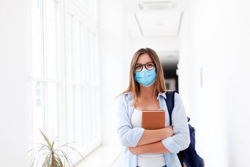 Student in protective face mask in empty college indoors. Young woman going to exams in high...