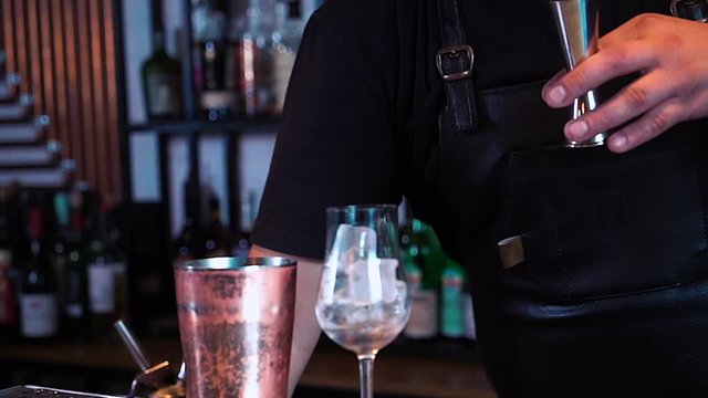 the barman's making a cocktail at the bar. The process of making a cocktail with alcohol. Someone's pouring liquid into the glass.