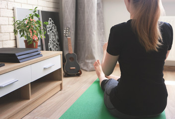 Young woman caucasian ethnicity practices yoga and stretching on green exercise mat at home. Concept training in living room. Healthy lifestyle, sport and fitness