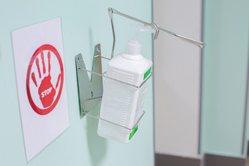 Hand sanitazing with antibacterial bittle and stop sign on the wall in hospital