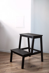 handmade wood furniture , a brown wood step ladder stands in a room with white walls and a brown floor,