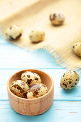 Many quail eggs in bowl with sackcloth on brown background