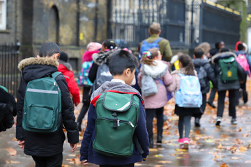 Happy primary asian, india, Chinese, africa & american Caucasian student, kids, pupils & teacher carrying  school bags on their way in rain winter day, with red maple leaves