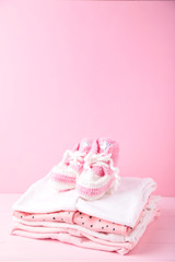 Baby clothes with booties on pink background with copy space