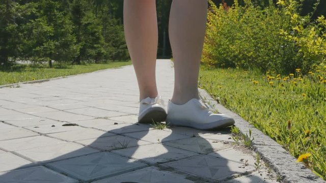 A young woman walks along the path, then she takes off her shoes and steps barefoot into a clearing with green grass and flowers. Concept of connection with nature. 4K