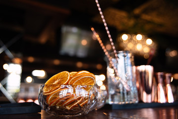 dried oranges lie in a glass vase, fruits are sliced ??in circles, beautiful light, close-up, a glass glass in the background, glare and lights in the background, a bar, restaurant, bar,