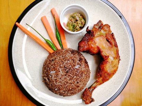 A fermented bean paste rice, a fried chicken thigh, green chilis, carrots and a side dish