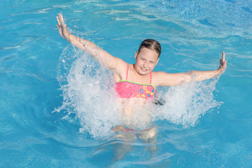 naughty game with water in an outdoor pool at a summer resort. a happy girl in a bright swimsuit jumps in the water with splashes from her hands. Summer vacation and healthy lifestyle concept