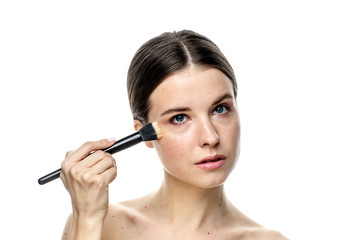 Fototapeta premium close-up portrait of a girl without makeup with clean skin with a makeup brush in hand, isolated on a white background