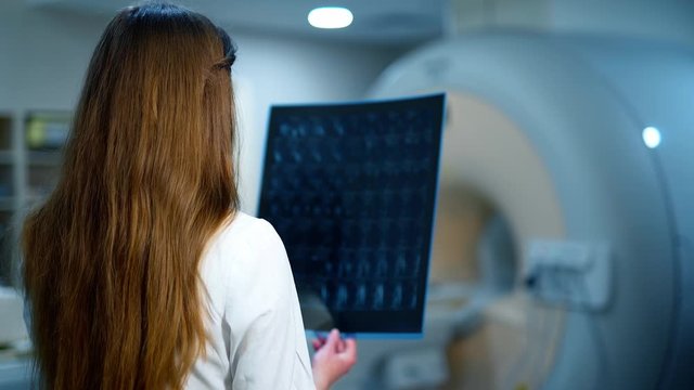 Medic examines x-ray in a contemporary clinic. Backside view of a female doctor holding radiogram picture. Medical concept.