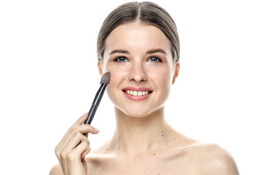 close-up portrait of a young brunette girl with blue eyes with clear skin, doing makeup with makeup brushes, isolated on a white background. High-resolution photos