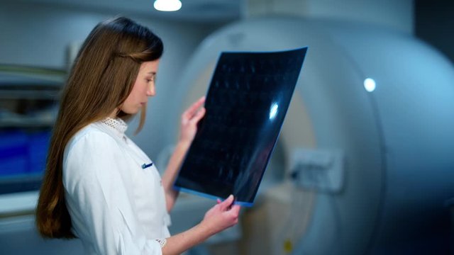 Young doctor radiologist looks at an x-ray in clinic. Female medic in uniform holding in hands and examines a radiogram picture of a patient.