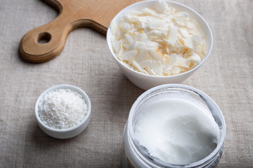 Bowl of coconut flakes and jar of coconut oil on fabric background. Superfoods.