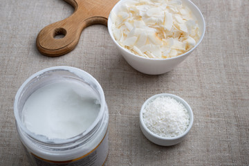 Bowl of coconut flakes and jar of coconut oil on fabric background. Superfoods.