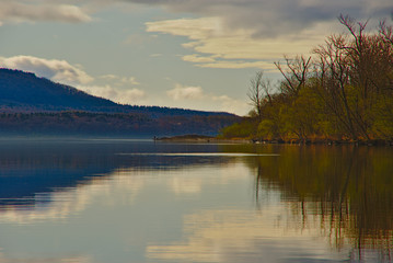 薄明の湖の風景。湖面に映る空。湖畔の森。屈斜路湖、北海道、日本。