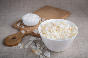 Coconut chips and shavings in a bowl on a cloth tablecloth and cutting board