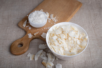 Coconut chips and shavings in a bowl on a cloth tablecloth and cutting board