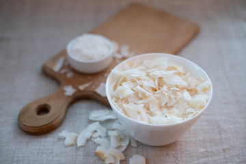 Coconut chips and shavings in a bowl on a cloth tablecloth and cutting board