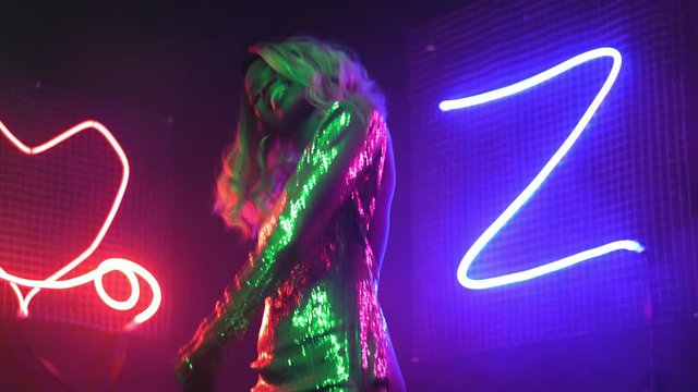 An African American woman is dancing in the neon lights of a nightclub or private party at home in a silver sequin dress with neon figure lights background. Neon concept. Prores 422. 