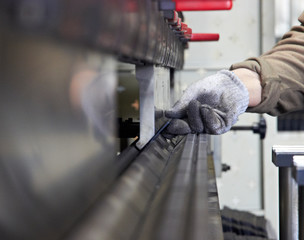 worker produces steel details on a metal bending equipmet