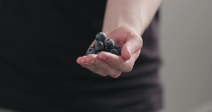 Slow motion man hand show big ripe blueberries on neutral background