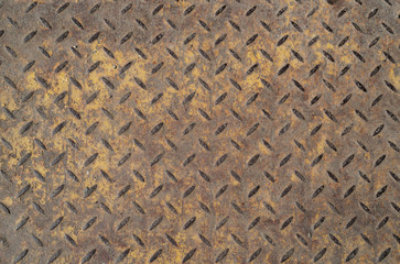 Old, rusty industrial metal floor with diamond pattern and residual yellow paint on the surface....