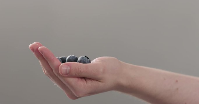 Slow motion man hand show big ripe blueberries on neutral background
