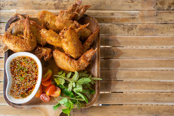 Fried wing chicken with sauce in wooden dish on bamboo table.