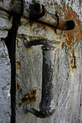 Old rusty handle with latch on gray cracked door surface of abandoned house 