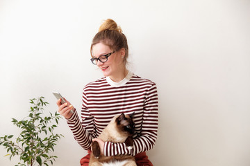 Young woman uses a smartphone with a cat on a white background in the room