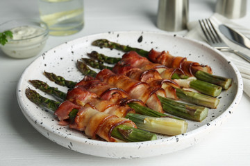 Oven baked asparagus wrapped with bacon on white table, closeup