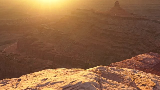 Two unrecognizable female tourists sitting on edge of cliff enjoying warm sunset in Dead Horse Point State Park, Utah, USA. Steadicam shot, UHD